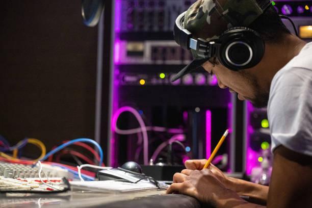 A young New Zealand rapper putting his idea into a song in a recording studio In a modern recording studio, a young New Zealand rapper using a pen and a piece of paper to create his own song. A inspiring and concentrate moment. Sound and  Music Promotion stock pictures, royalty-free photos & images